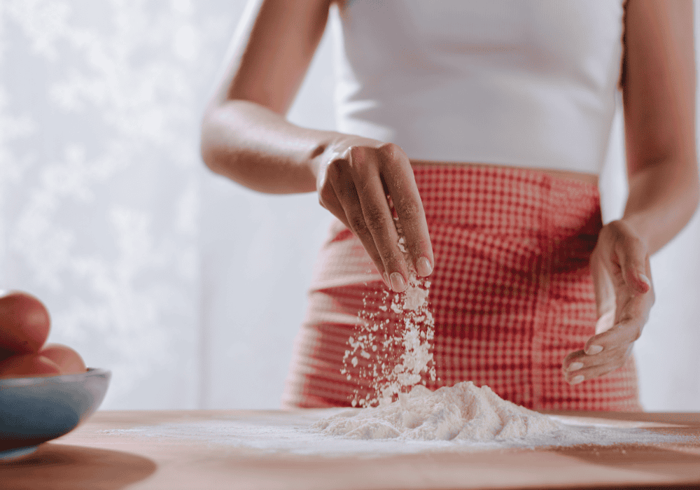 A woman in red and white is making something out of flour.