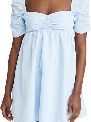 A woman wearing light blue dress standing next to wall.