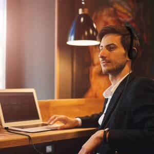 A man sitting at a table with headphones on and looking at his laptop.