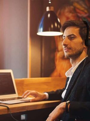A man sitting at a table with headphones on and looking at his laptop.