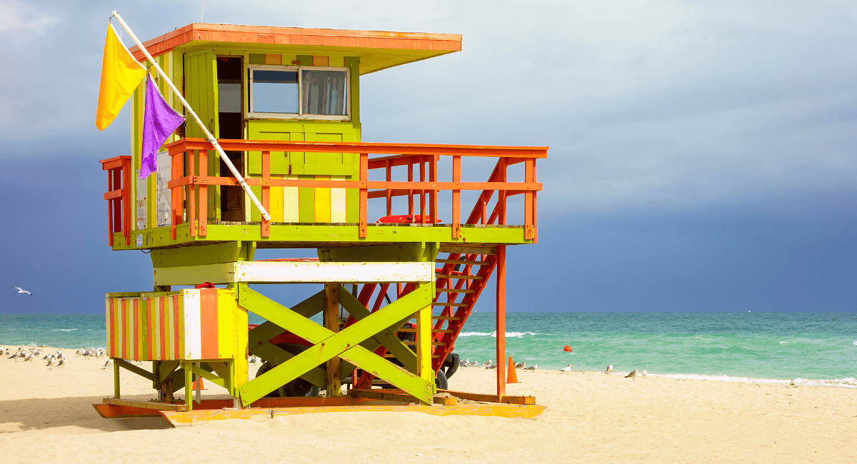 A lifeguard tower on the beach with people standing around.