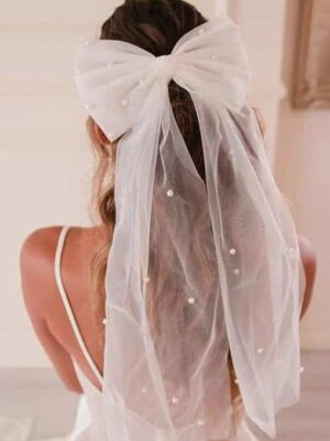 A woman in white dress with veil and bow.