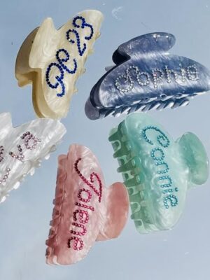 A group of different colored hair clips with names written on them.
