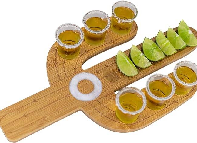 A wooden tray with six shots of alcohol and lime slices.