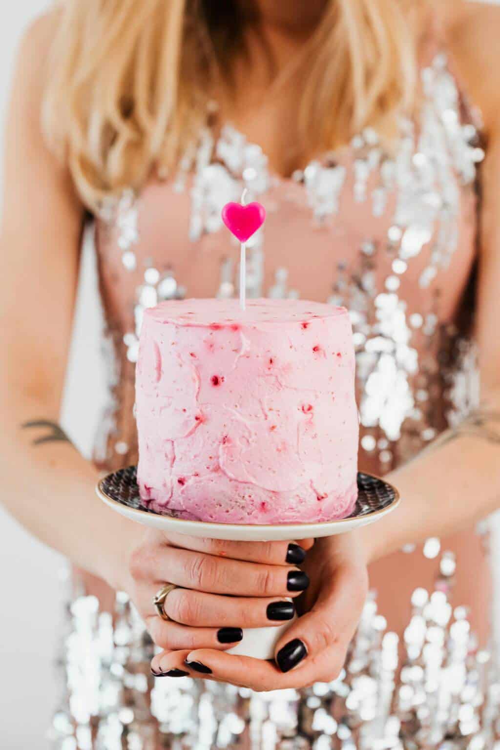 A woman holding a pink cake with sprinkles on it.