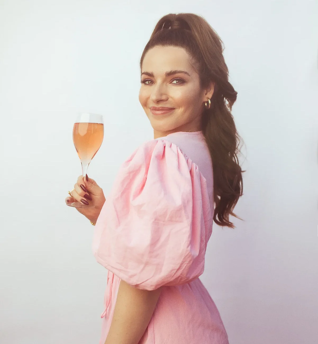 A woman in pink holding a glass of wine.