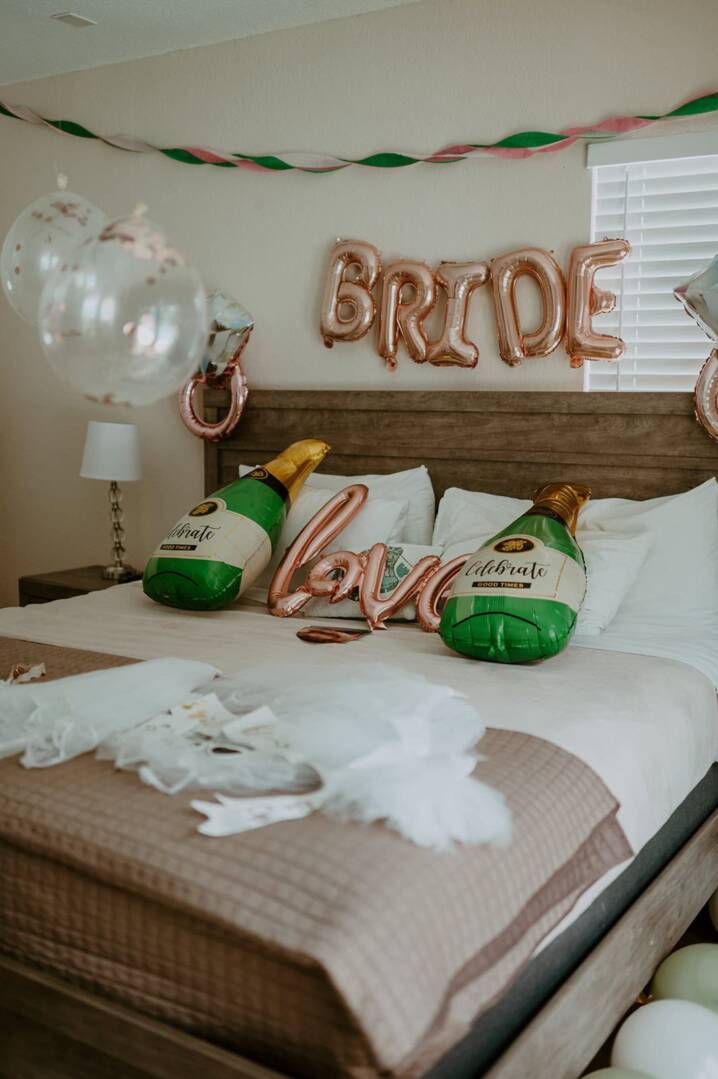 A bedroom with balloons and champagne bottles on the bed.