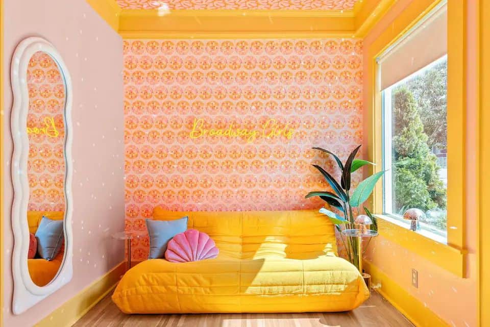 A yellow couch in front of a pink wall.